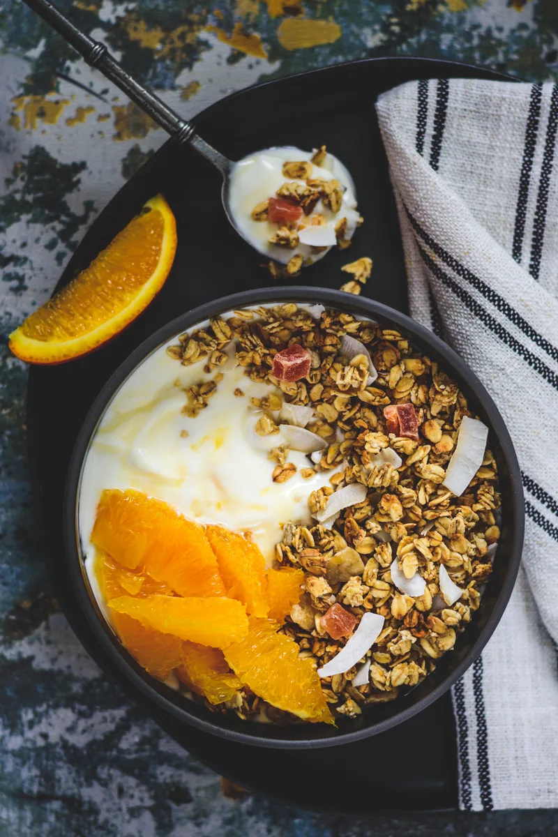 Een kom yoghurt met granola en sinaasappel