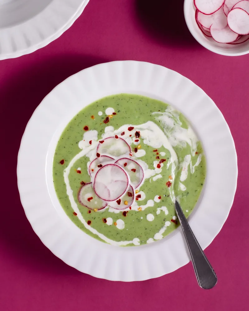 Een kom groene soep met radijs op een roze ondergrond