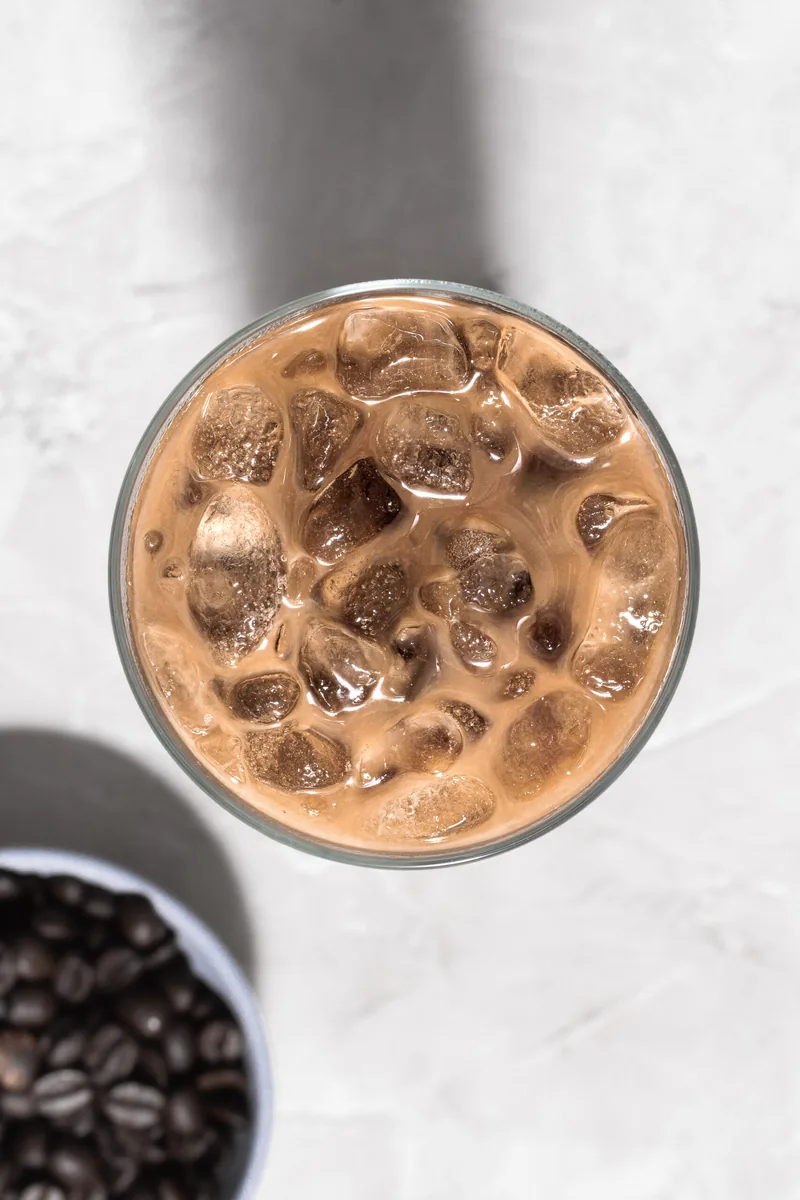 Een glas ijskoffie van boven, met koffiebonen ernaast