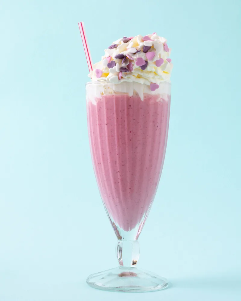 Een roze milkshake met slagroom in een hoog glas