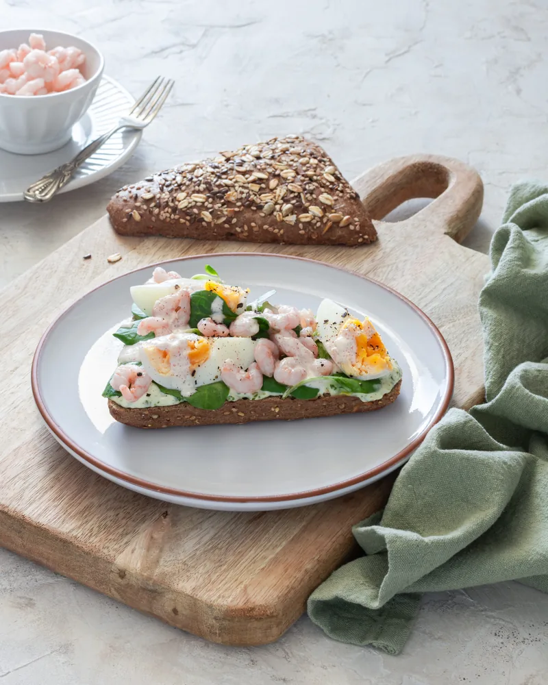 Een belegde boterham met ei en garnalen op een houten plank