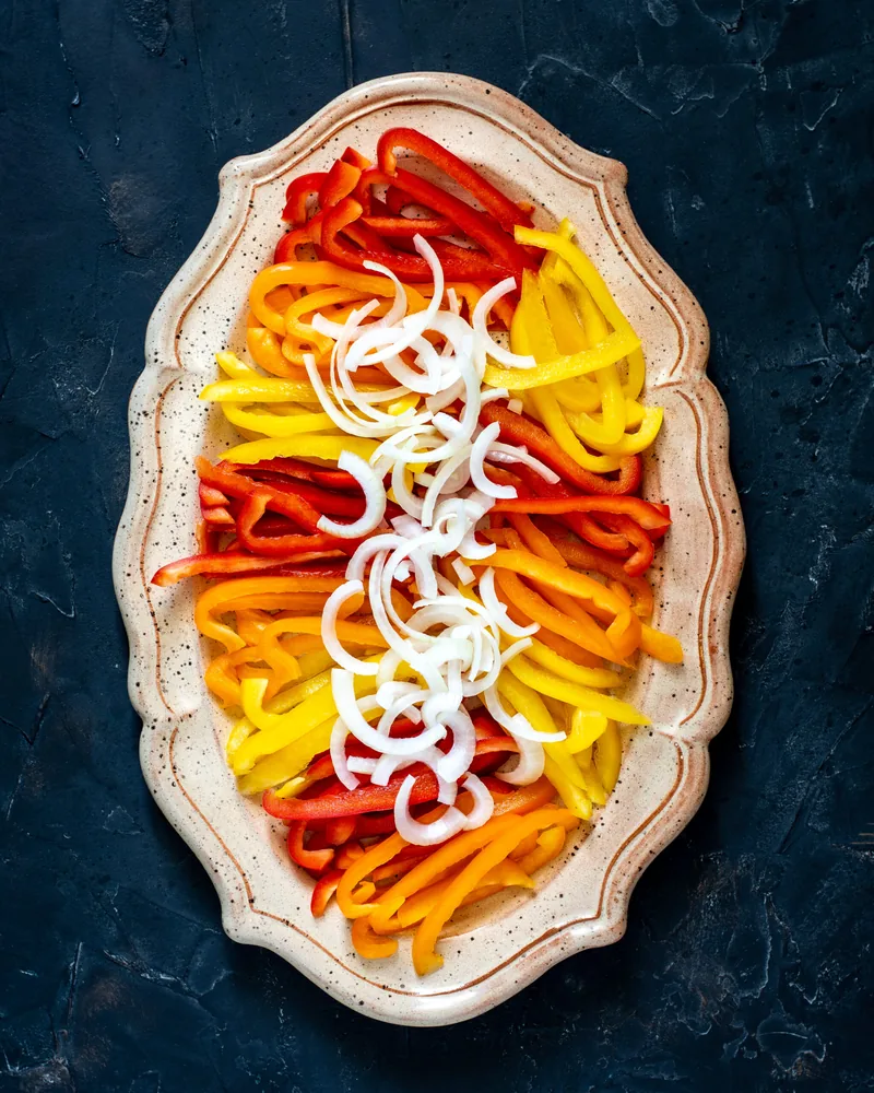 Een schaal met reepjes rode, oranje en gele paprika