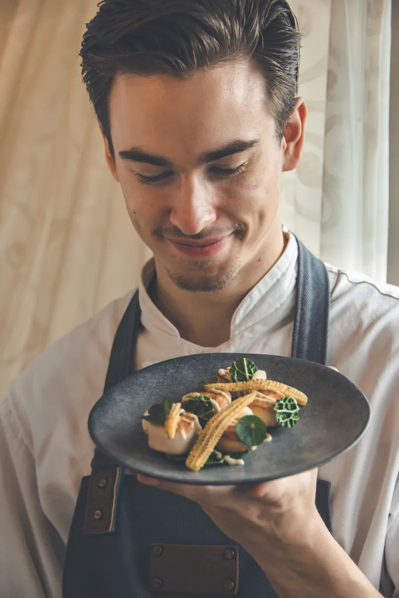 Een kok houdt lachend een bord met een gerecht omhoog
