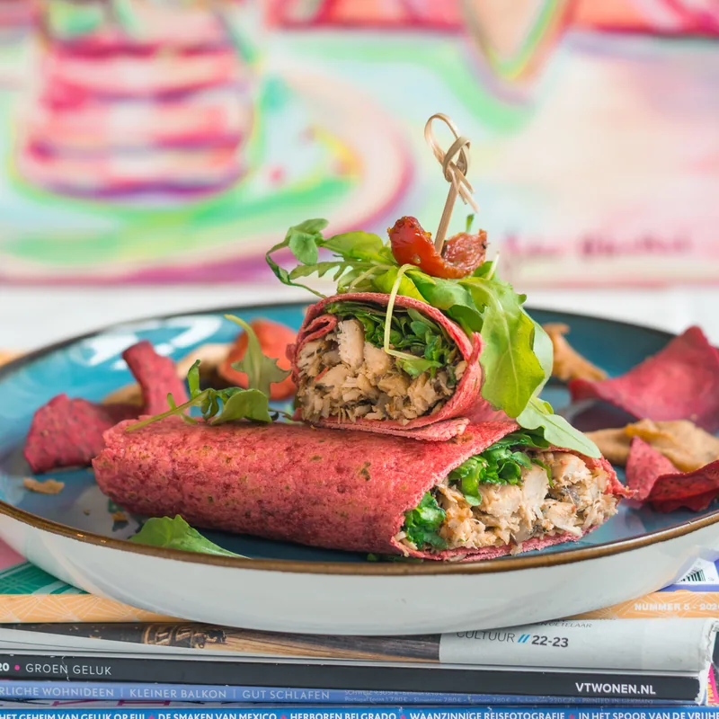 Een roze wrap met kip en sla op een blauw bord